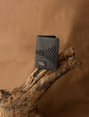 Black textured leather wallet with stitched triangular pattern and logo on natural wooden branch