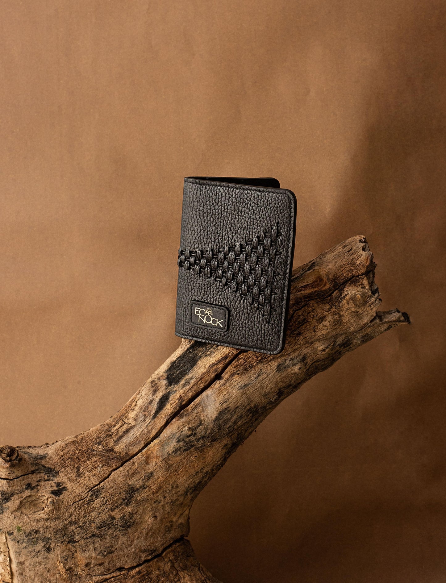 Black textured leather wallet with stitched triangular pattern and logo on natural wooden branch