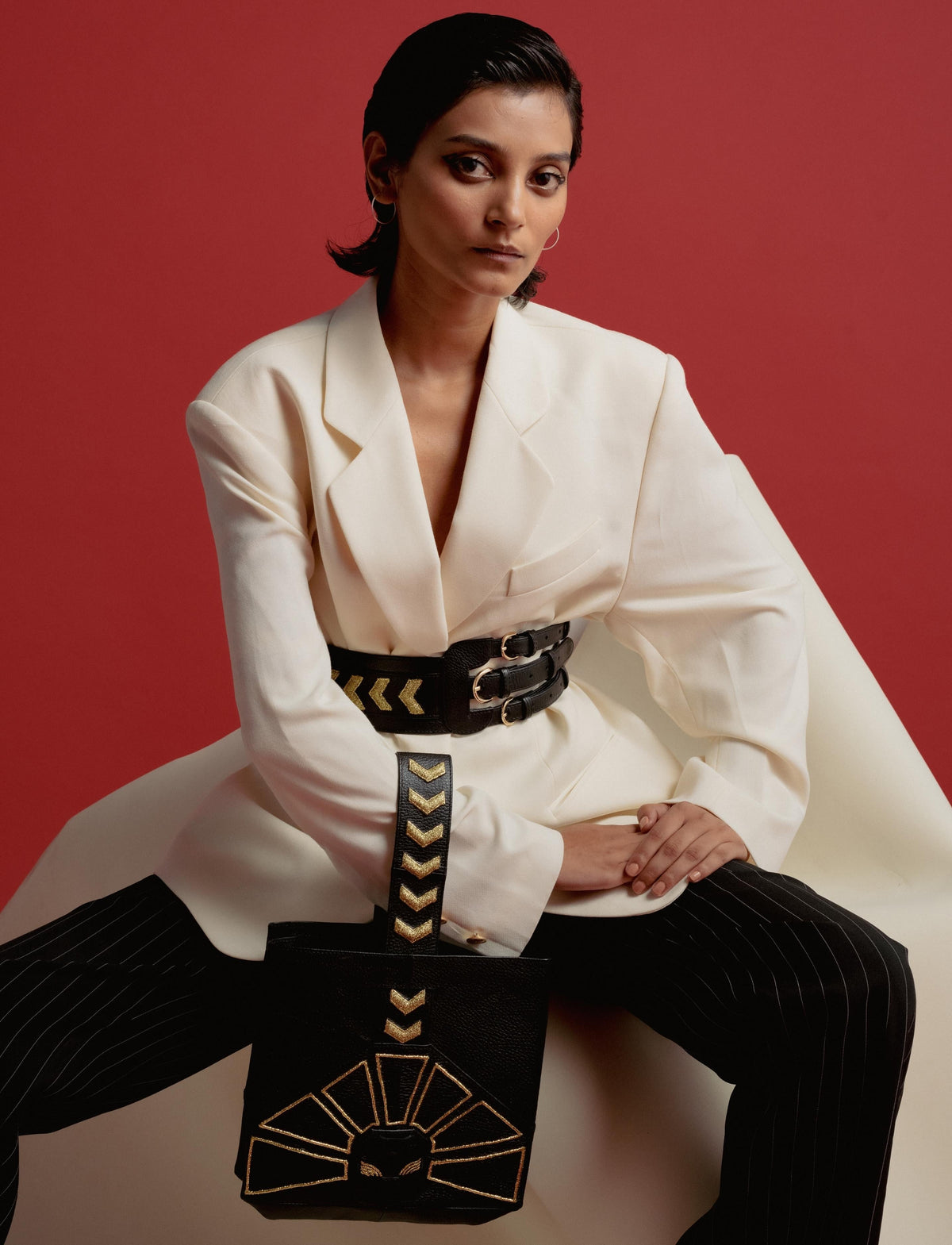 Stylish woman in oversized white blazer with black belt and pinstripe pants holding black bag with gold design