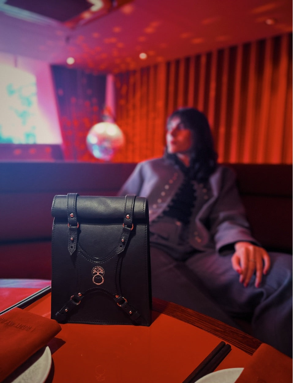 Black leather handbag on red table with blurred woman in gray outfit in stylish lounge