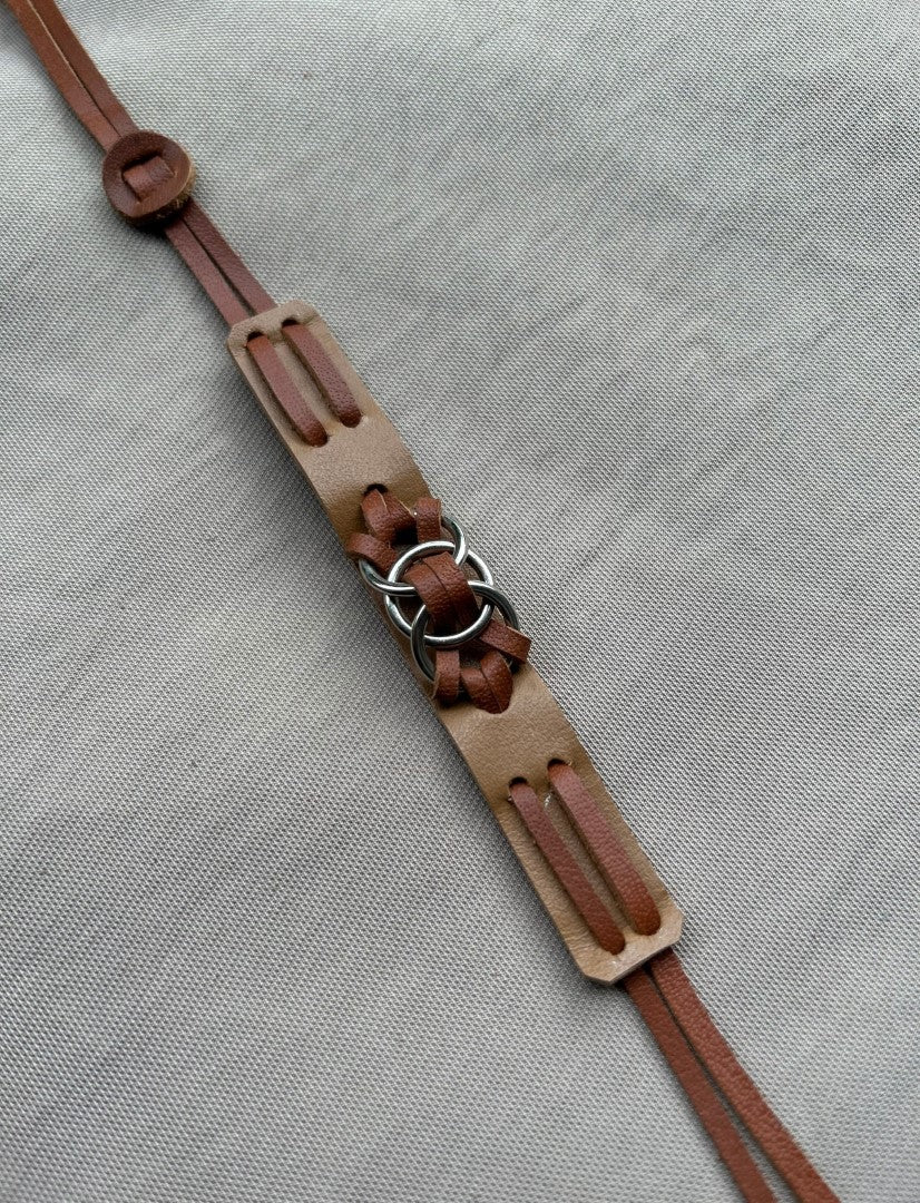 Brown leather strap with metal rings laid on textured gray fabric