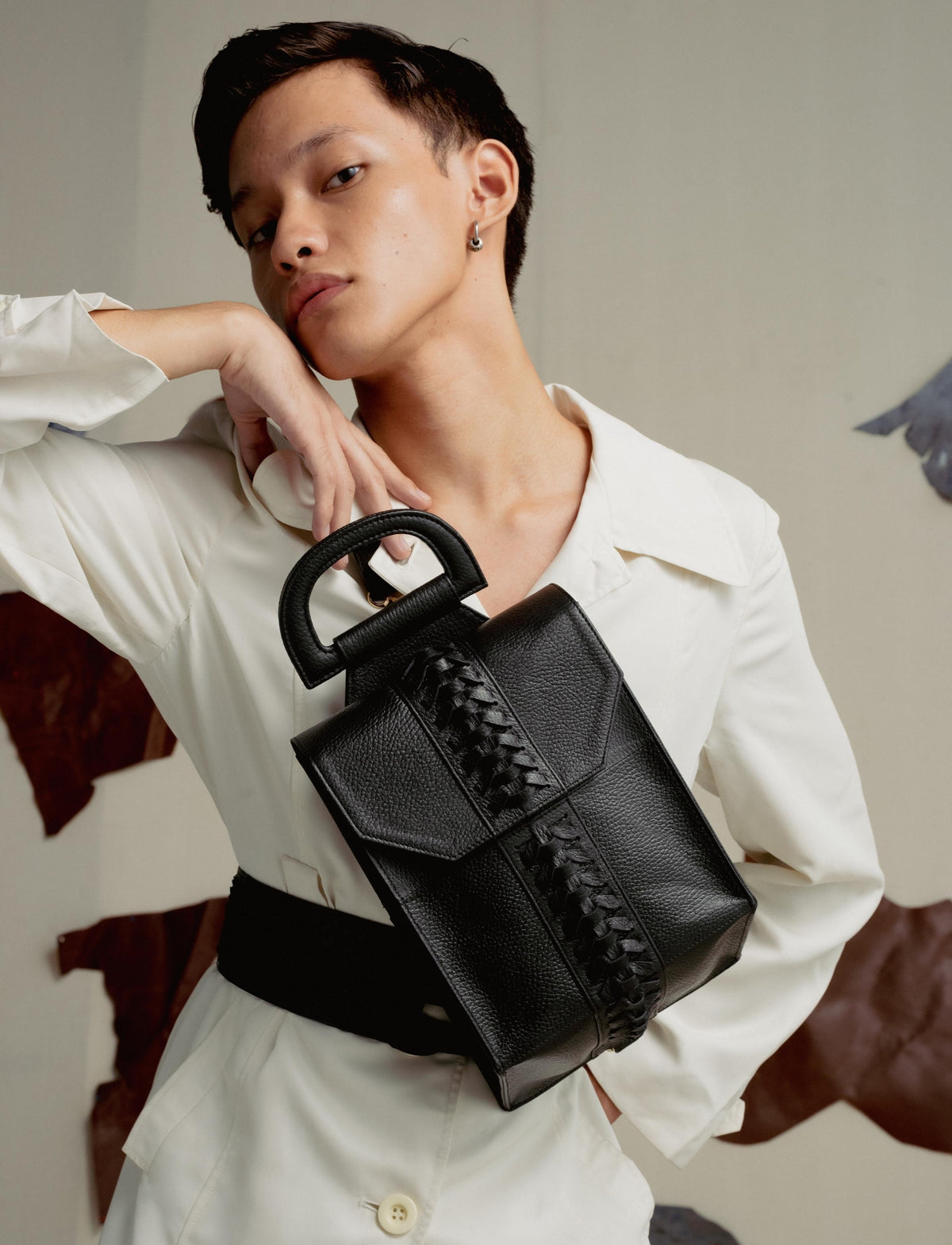 Stylish person in white outfit posing with a black leather handbag with braided detail