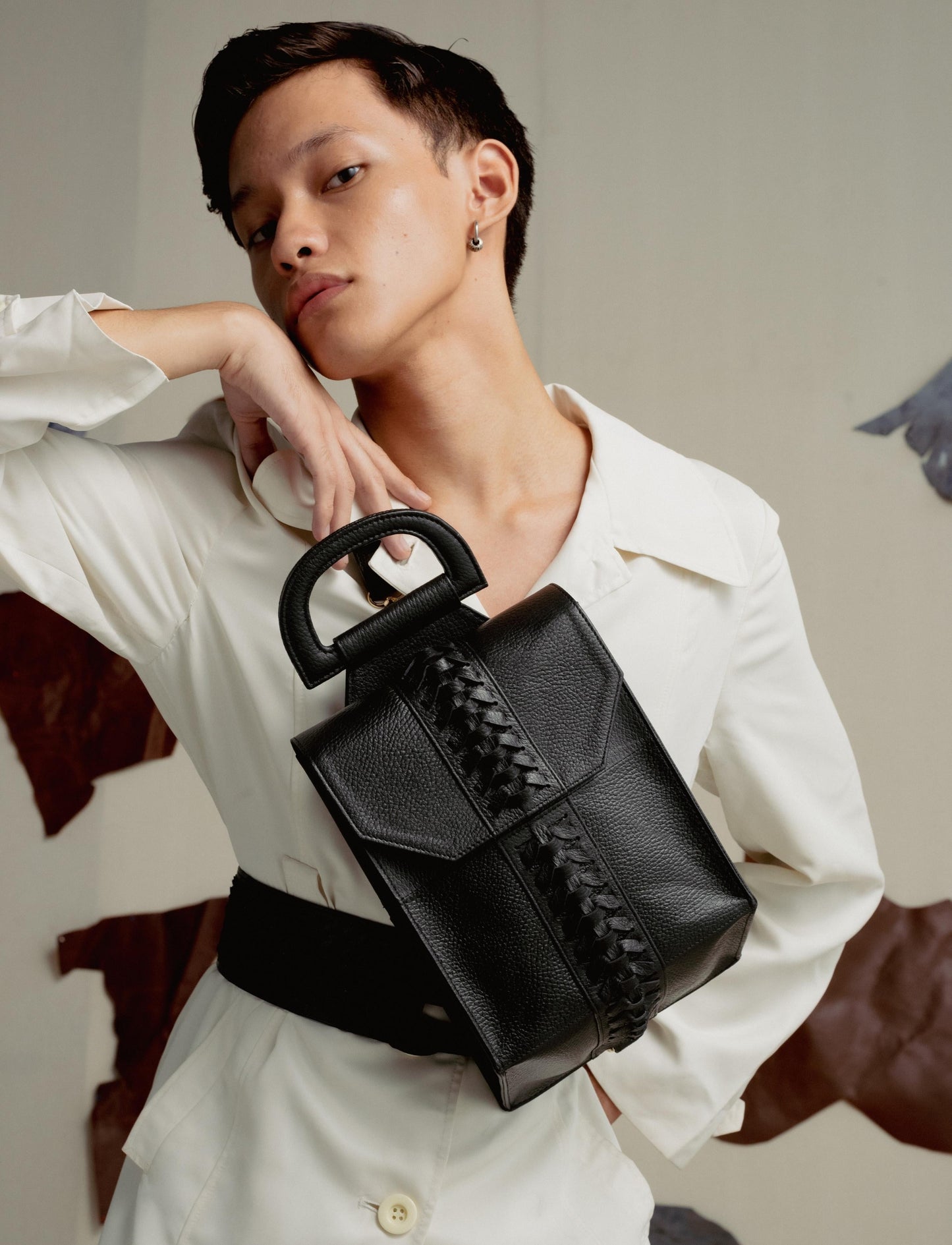 Stylish person in white outfit posing with a black leather handbag with braided detail