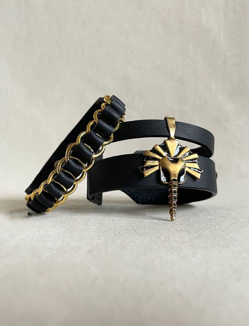 Two black leather bracelets with gold accents, one with linked gold rings and the other with a gold lion head charm