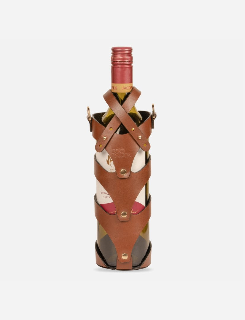 Wine bottle secured in tan stitched upcycled leather case with brass studs on white background