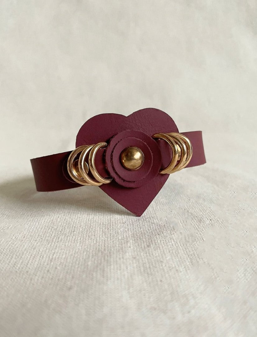 Timeless burgundy leather cuff bracelet with gold ring studs and heart centerpiece on light fabric