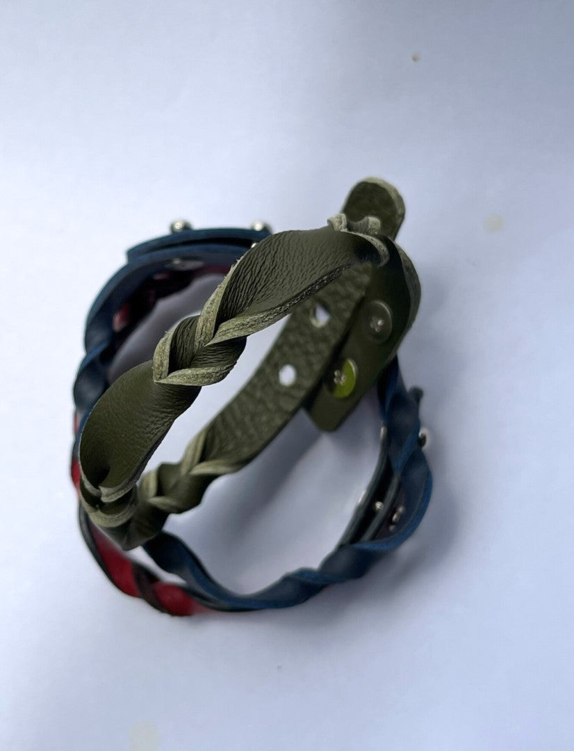 Close-up of two braided leather bracelets, one olive green and one dark blue with red accents, against a white background