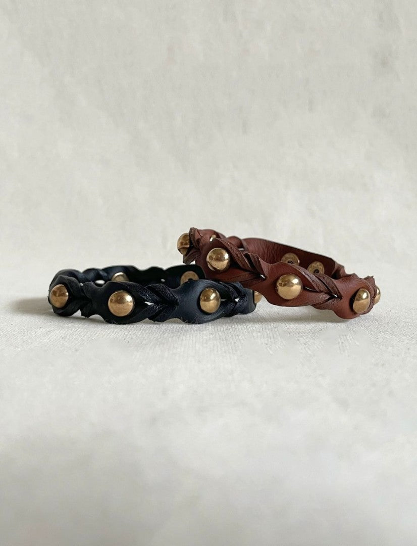 Handcrafted black and brown leather cuff bracelets with gold metallic studs on a neutral fabric background