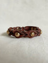 Handcrafted tan leather bracelet with braided design and gold metallic studs on beige fabric