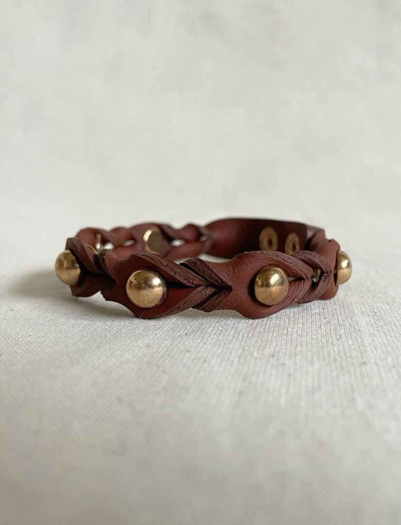 Handcrafted tan leather bracelet with braided design and gold metallic studs on beige fabric
