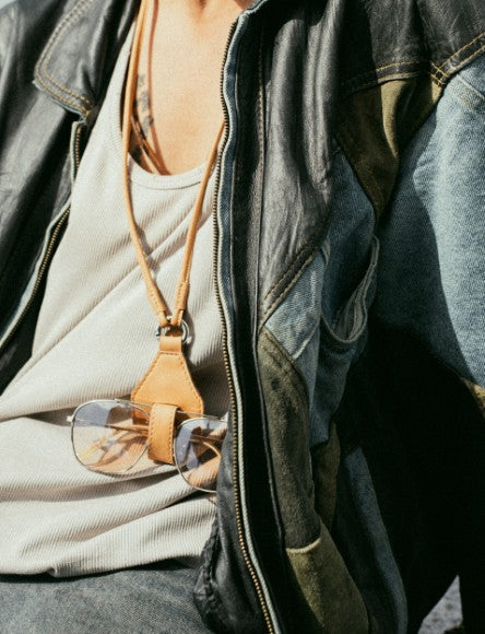 Close-up of person wearing white tank top and black leather jacket with sunglasses hanging on tan leather strap