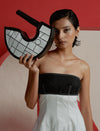 Woman in black and white strapless dress holding unique black and white semicircle handbag against red and beige background