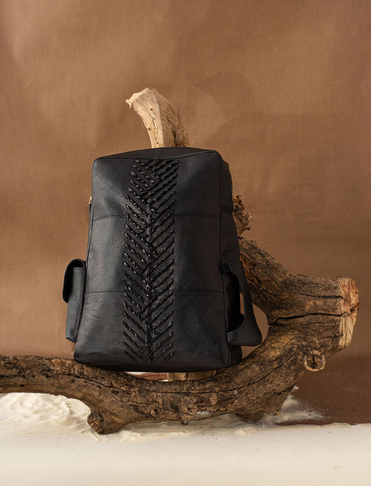 Designer Black leather backpack with braided detailing displayed on a rustic wooden branch against brown background