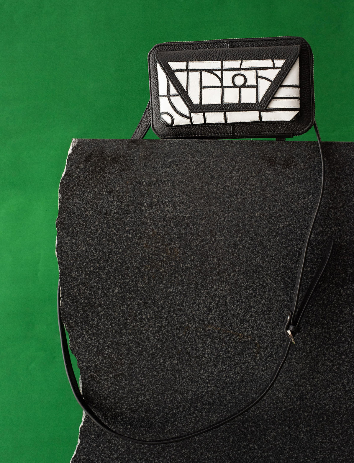 Black and white geometric-patterned leather crossbody bag on black stone with green background