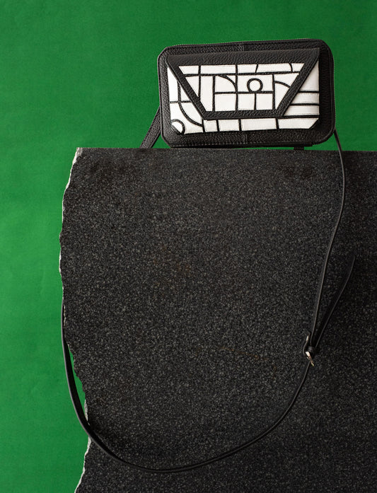Black and white geometric-patterned leather crossbody bag on black stone with green background