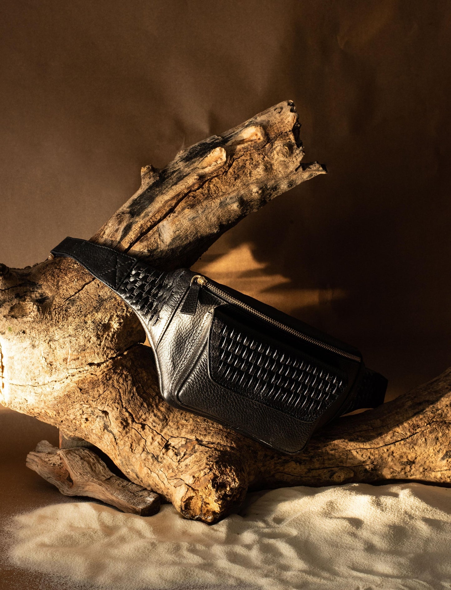 Black leather textured crossbody bag displayed on rustic wood with sand backdrop