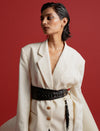 Woman in white oversized blazer with gold buttons and black woven belt against red background