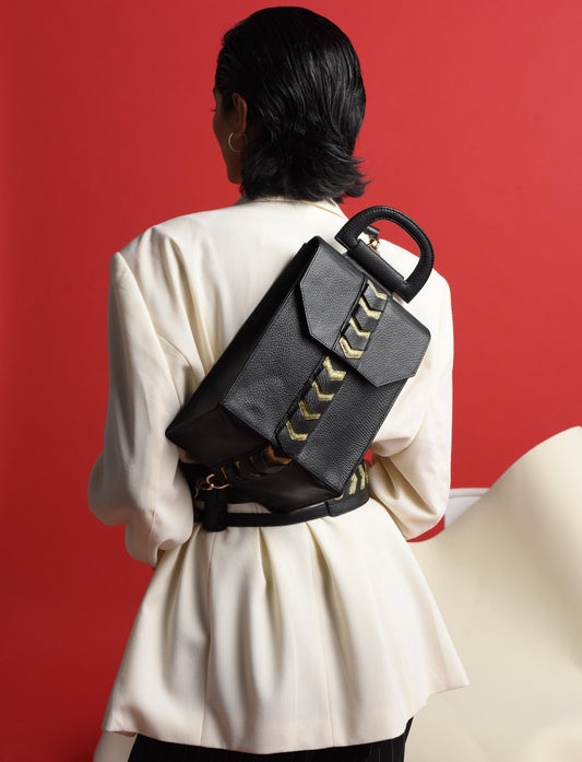 Back view of woman in white blazer wearing black leather backpack with gold arrow detail against red background