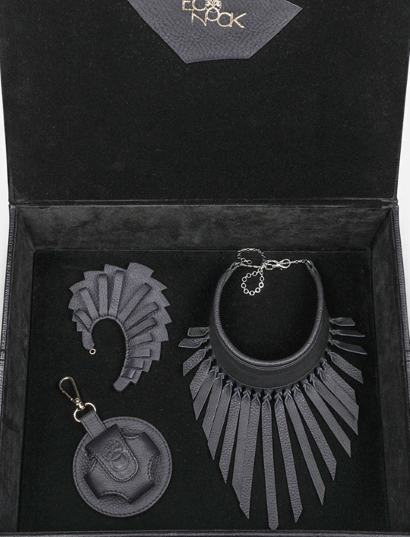 Elegant black leather jewelry set with fringe necklace, matching earrings, and round keychain in a black velvet box