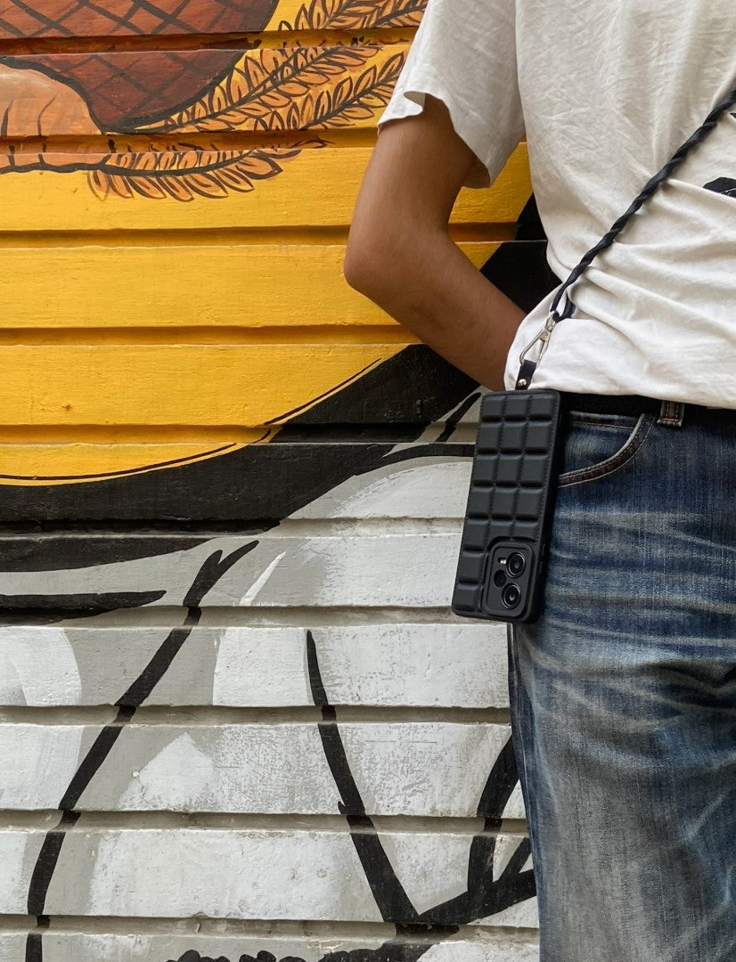 Person wearing blue jeans and white shirt with a black quilted phone sling against colorful graffiti wall