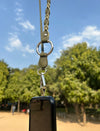 Timeless olive green leather phone sling with silver hardware hanging outdoors against a clear blue sky and green trees