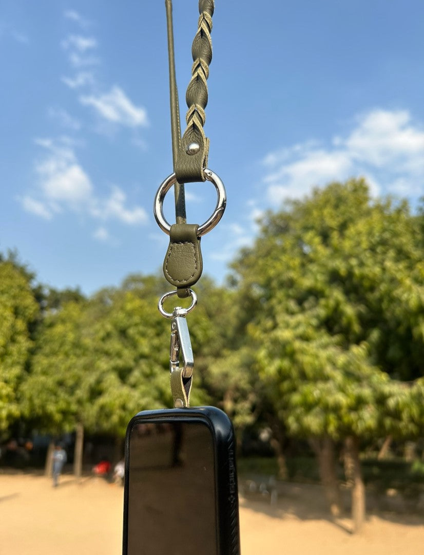 Timeless olive green leather phone sling with silver hardware hanging outdoors against a clear blue sky and green trees