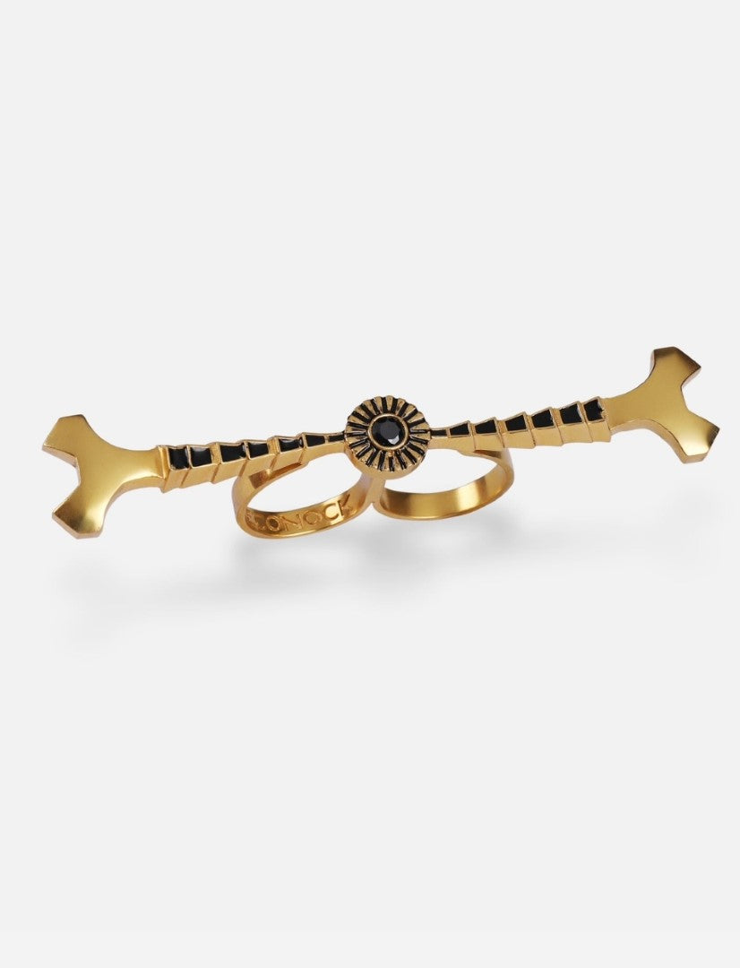 gold-tone metal double finger ring with black enamel detailing and stud accents on white background