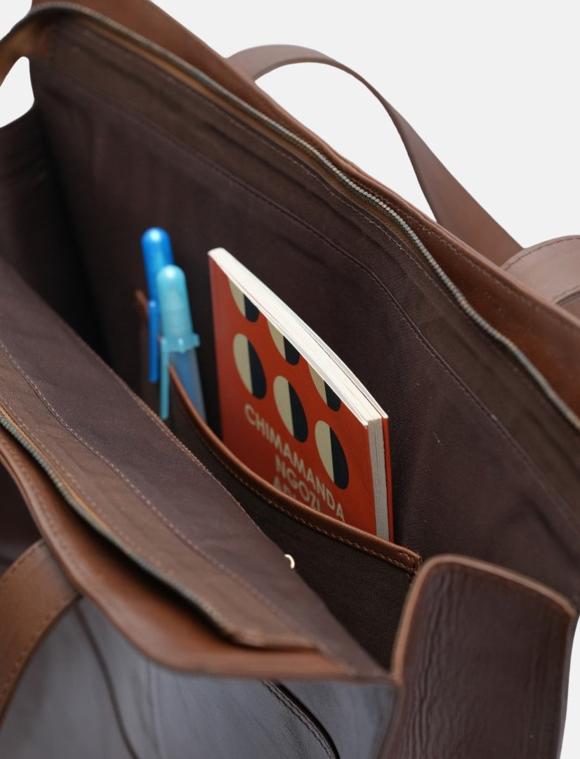 Brown leather tote bag interior showing a pocket with a book and two blue pens inside