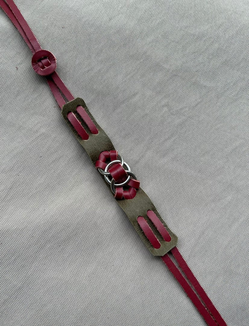 Handmade leather bracelet with burgundy straps and metal rings on gray fabric background