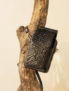 Black leather textured crossbody bag hanging on rustic wooden branch background