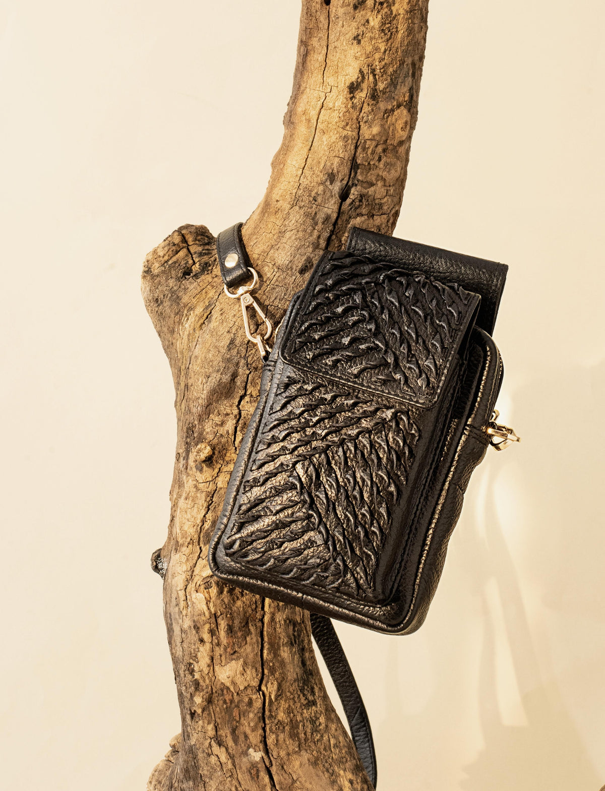 Black leather textured crossbody bag hanging on rustic wooden branch background