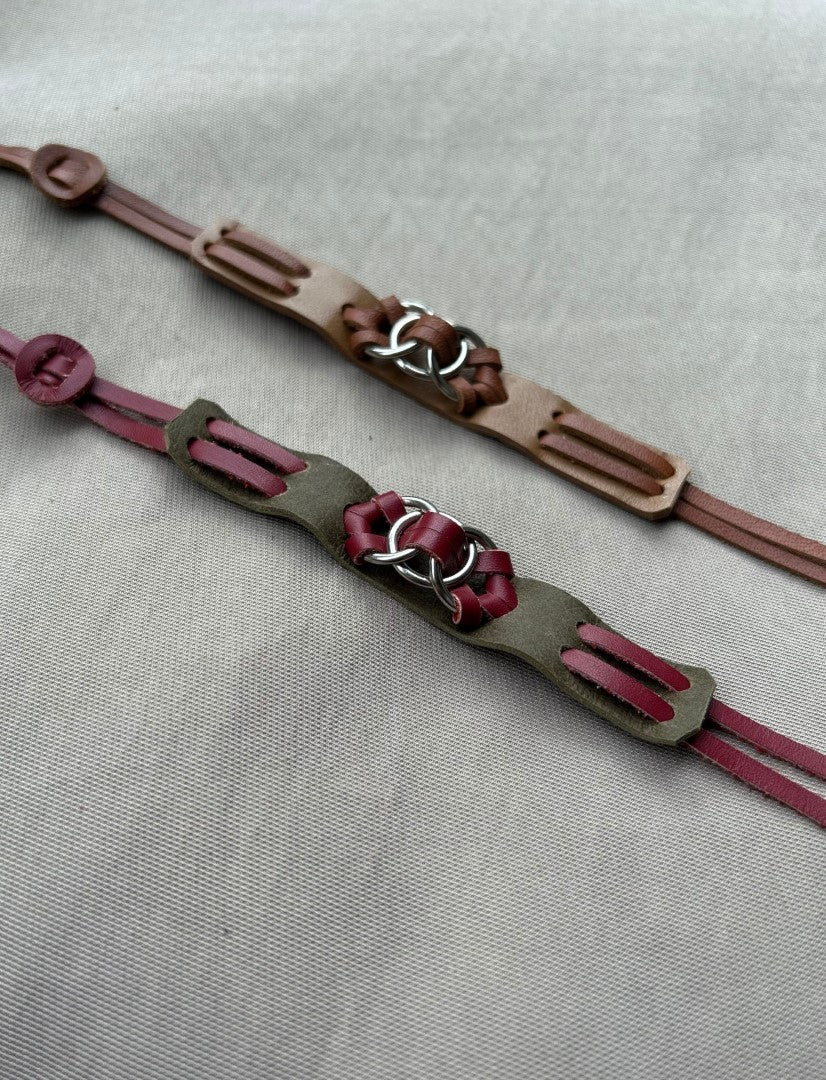 Two handmade leather bracelets with metal ring accents on neutral fabric background