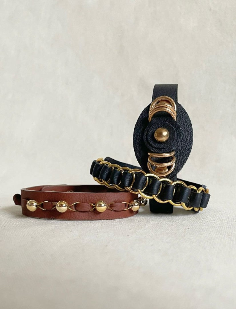 Handcrafted men's black and brown leather bands with gold ring studs on a neutral fabric background