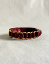 Timeless burgundy leather men's band bracelet with upcycled gold ring studs on beige fabric background