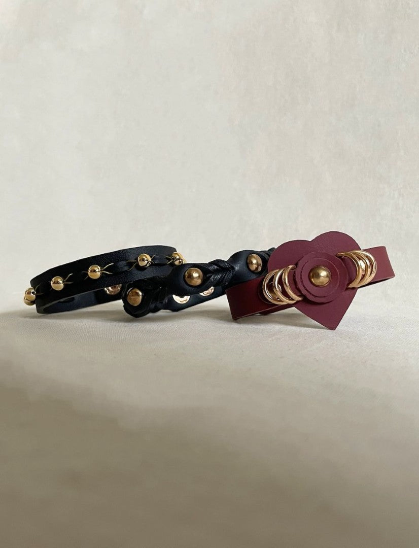 Three handcrafted leather bracelets with gold beads and rings on a plain beige background