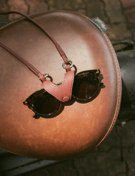 Brown leather sunglasses holder securing black sunglasses on a brown leather bike seat