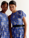 Two women wearing blue floral plaid dresses with puffed sleeves and black belt, posing against white background