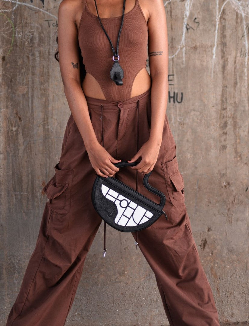 Person wearing brown tank top and high-waisted brown cargo pants holding black and white geometric handbag