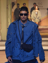 Male model in blue layered jacket and shirt with black tie and sunglasses on runway