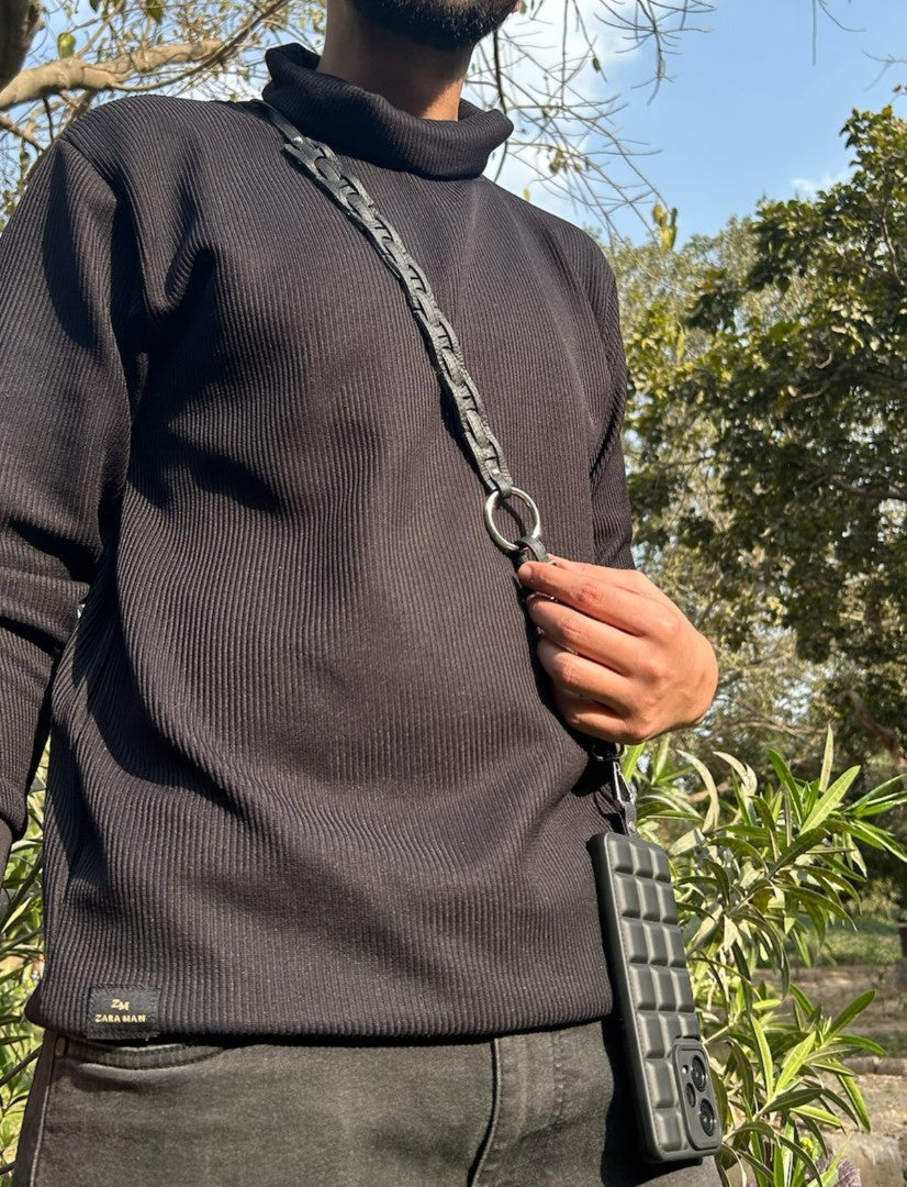 Man wearing black Zara black sweater holding a black textured phone sling with upcycled leather strap outdoors