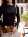 Woman wearing black top with handmade tan leather woven wristlet and crossbody bag in outdoor setting