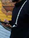 Man wearing black turtleneck with timeless ivory white braided leather phone sling around neck, holding a smartphone