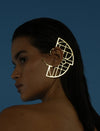 Profile of woman with sleek dark hair wearing large gold geometric metal ear cuff against blue background