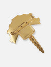 Back view of a gold metal brooch shaped like a key with a pin fastening on white background