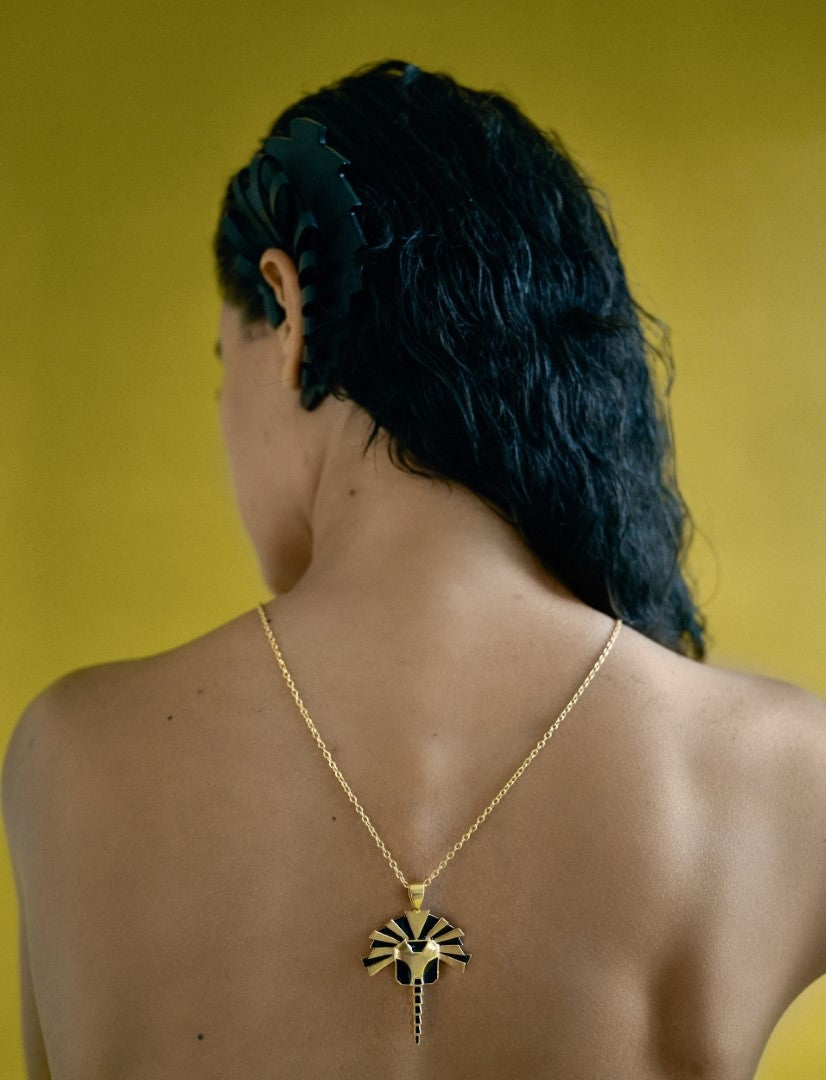 Woman with wet hair against yellow background wearing gold necklace with black enamel lion pendant