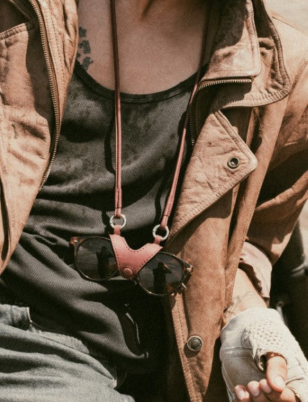 Close-up of person wearing brown leather jacket, black tank top, and sunglasses hanging by leather strap