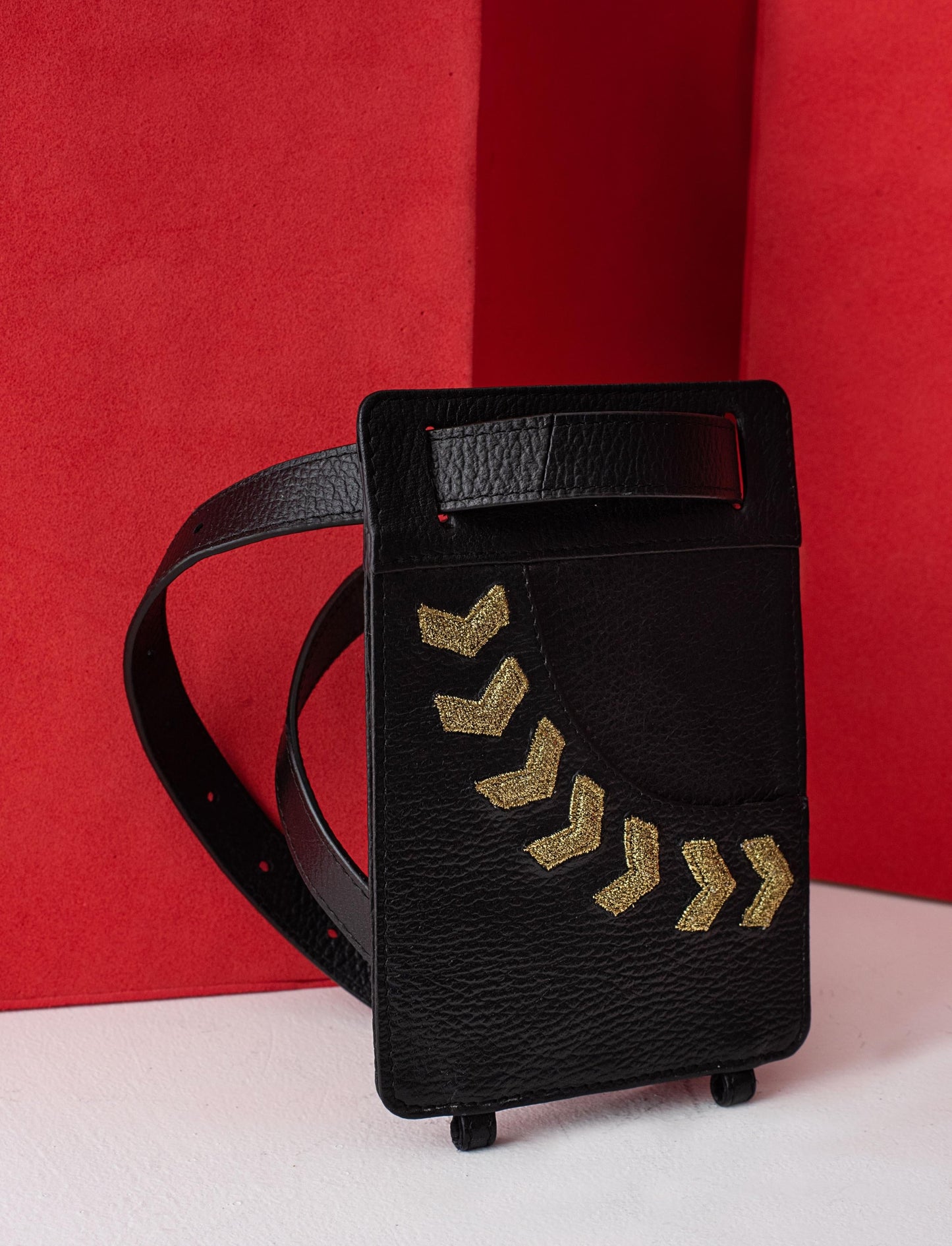 Black leather belt bag with gold chevron embroidery against red and white background