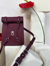 Maroon leather backpack with silver hardware and a rolled top, displayed on white foam blocks with a red anthurium flower