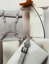 Minimalist beige leather handbag with silver buckle and embossed logo, displayed on white foam blocks with red flower