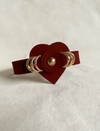 Timeless tan leather cuff bracelet with heart centerpiece and gold rings on white fabric